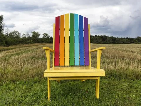 Yellow wooden chair back painted in rainbow colours standing in a meadow Stock Photos