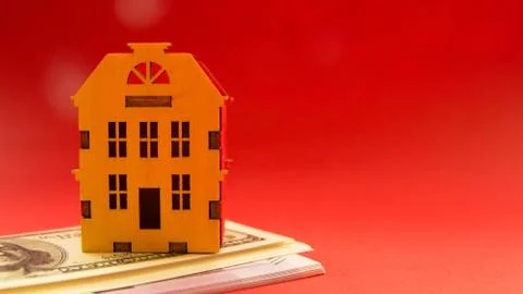 Yellow wooden model house on stack with money on red background with copy spa Stock Photos
