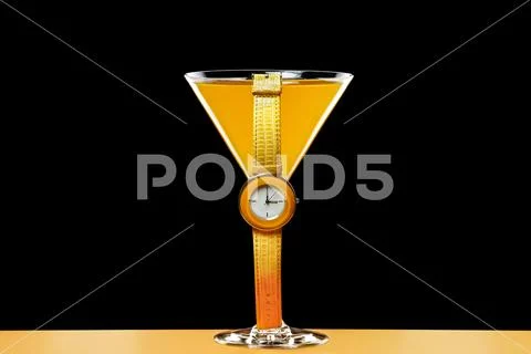 Yellow wristwatch and glass with drink on a black background Stock Photos