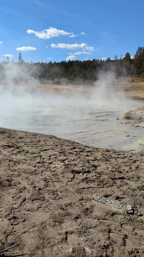 Yellowstone Mud Volcano Trail shows steaming mud pot and blue sky Stock Footage 321506900