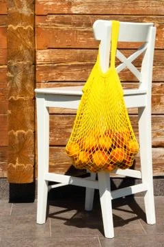 Yelow mesh bag or string bag with ripe peaches on the back of a white chair Stock Photos