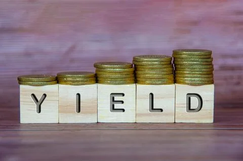 Yield text on wooden cubes with stacking golden coins. Business concept Stock Photos