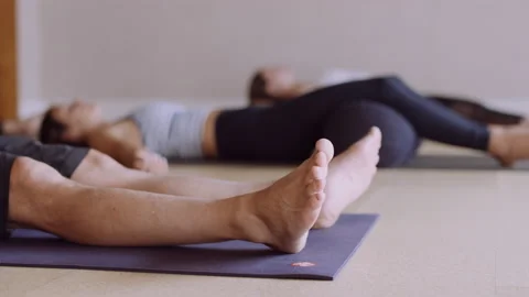 Yoga class does shavasana pose in studio, rack focus from man's feet to woman Stockbeeldmateriaal 202762122
