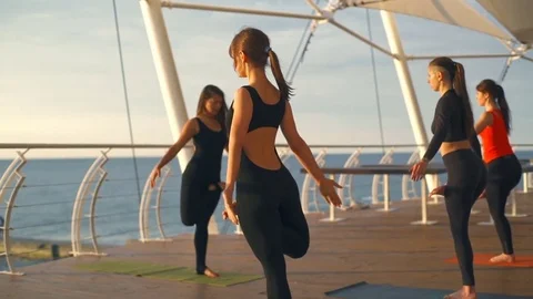 Yoga class group girl practice yoga Vriksasana tree Pose sunset sea slow motion Stock Footage 76933293