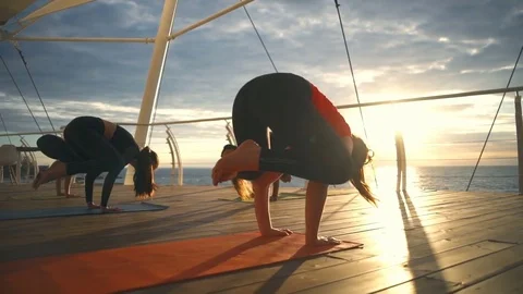 Young woman practicing yoga on the beach, doing crane pose