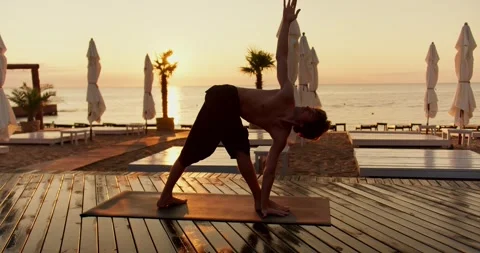 Yoga classes in the morning. Young guy doing yoga at sunrise on the beach Stock Footage 249435659