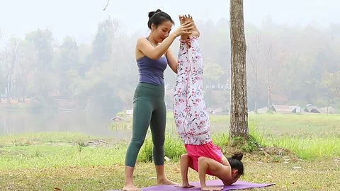 Yoga instructor assists adjusts student in Headstand on mat in outdoor park. Stock Footage 132108635