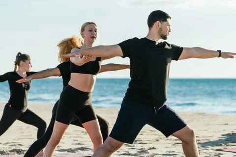 Yoga instructor correcting the pose of a man during a yoga class on a beach Stock Photos