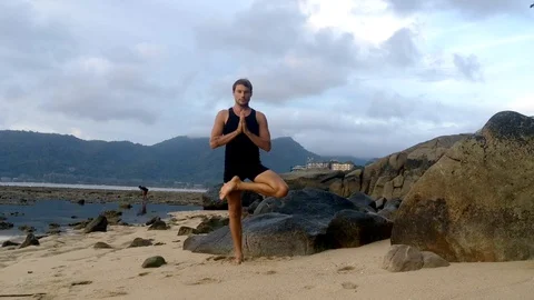 Yoga instructor demonstrates asanas exercises standing on rocky beach outdoors  Stock Footage 95166413