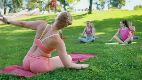 Yoga instructor demonstrating seated side stretch in park Stock Footage 279130878