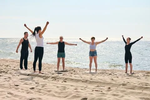 Yoga instructor leads group practice by Baltic Sea on sunny beach Stock Photos