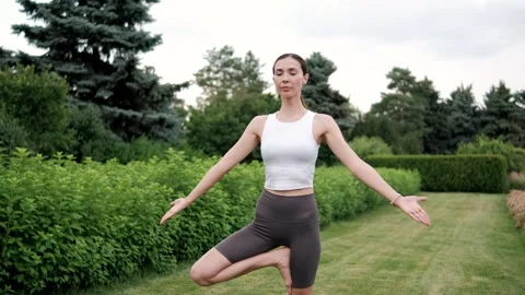 Yoga instructor practicing the tree pose in a serene garden setting, promoting Stock Footage 294892633