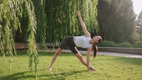 Yoga instructor practicing various poses outdoors beneath a willow tree Stock Footage 296209362