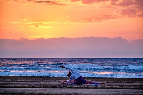 Yoga practice at sunset on the beach with waves in the background Stock Photos