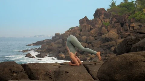 Yoga practitioner does sirsasana on sea coast slow motion Stock Footage
