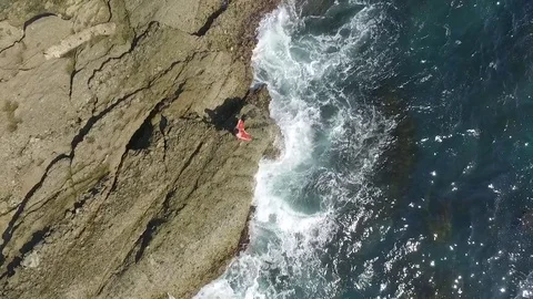 Yoga teacher doing yoga on the cliffs in the sea. Aerial drone view. Stock Footage 73685085