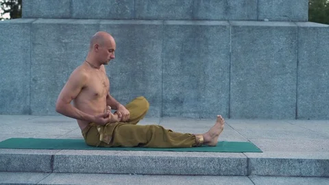 Yogi with Naked Torso Performs Asanas of Yoga on the Rug in City Park at Dawn Stock Footage 85329660