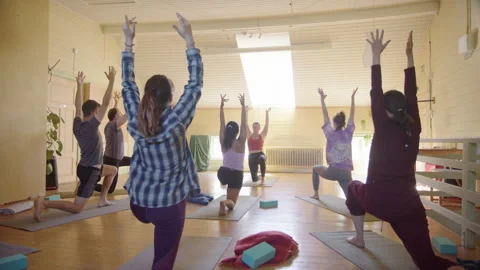 Yogis in class led by instructor go into Warrior 1 pose and then stretches Stock Footage 277622096