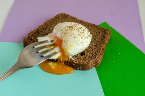 The yolk flows out onto a multi-colored table. Pieces of bread and ground pep Stock Photos