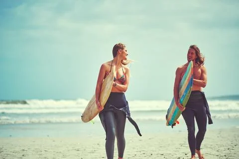 You can never go wrong with surfing. a young couple walking on the beach with Stock Photos