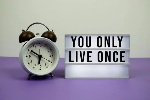 You Only Live Once text on LED lightbox with alarm clock on purple background Stock Photos