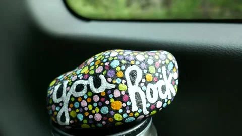 You rock kindness rock bouncing around on travel cup in car by window Stock Footage 293534881