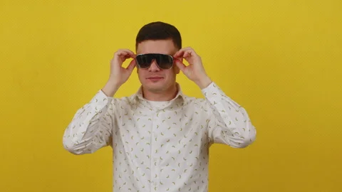 Young 20s guy posing on a yellow background in a white shirt and funny glasses Stock Footage 172039367