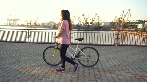 Young active brunette holding bycicle in her hand, while posing on camera Stock Footage 77764784