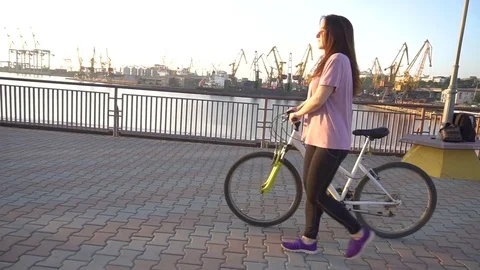 Young active brunette holding bycicle in her hand, while posing on camera Stock Footage 79064549