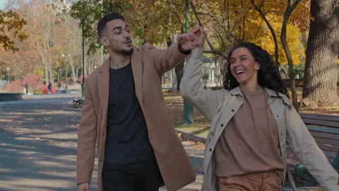 Young active hispanic couple walking holding hands hugging in autumn city park Stock Footage 166035054