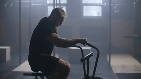 Young active man spinning air bike in gym. Male training on air bike in slow Stock Footage 124046962