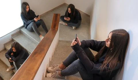 Young adolescent using mobile on stairs. Contemporary loneliness, mobile addi Stock Photos