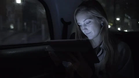 Young adult female in taxi using digital tablet at night Stock Footage