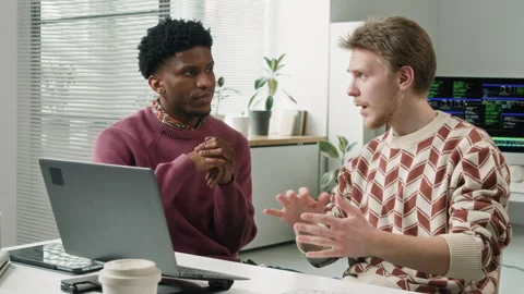 Young Adult Male Developer Explaining Code Bug to Colleague at Laptop in Office Stock Footage 330132033