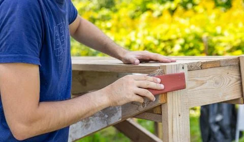 Young adult man hand using dark sandpaper sponge and sanding light wooden sur Stock Photos
