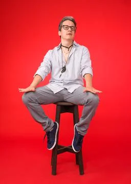 Young adult seated on high stool. red background Stock Photos
