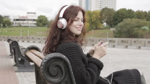Young adult woman in headphones using mobile phone outdoors Stock Footage