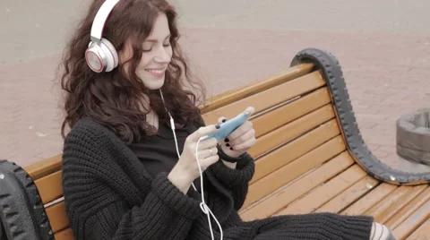 Young adult woman in headphones using mobile phone outdoors Stock Footage