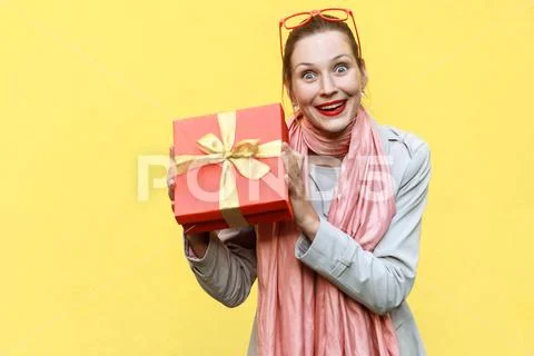 Young adult woman holding gift box and looking at camera and toothy smile. Stock Photos