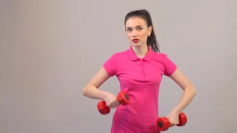 Young adult woman possing with dumbbells, sports pink clothing, fitness studio Stock Footage