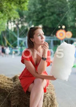 Young adult woman sitting on bale of hay and holding white cotton candy at am Stock Photos
