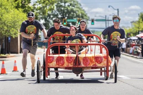 Young adults push bed down city street in fundraising event Foto stock