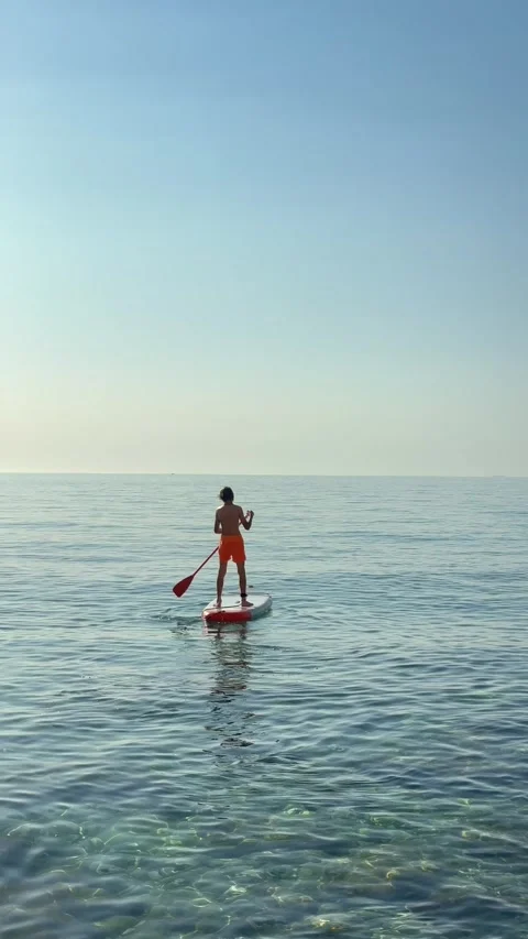 Young adventurous boy stand-up paddleboarding alone on the open turquoise s.. Stock Footage 338443998