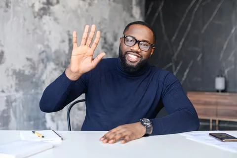 Young affable man sitting at the table welcoming Stock Photos