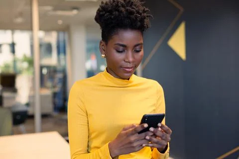 Young african american businesswoman text messaging through smartphone at Stock Photos