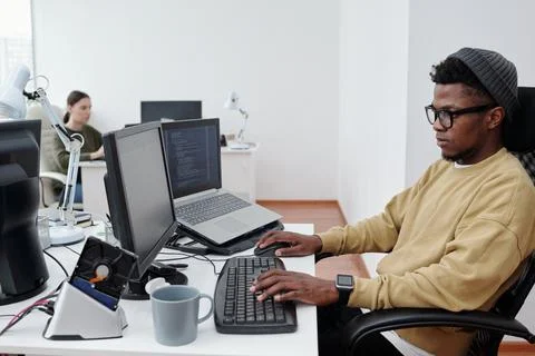 Young African American it developer in casualwear decoding data in office Stock Photos