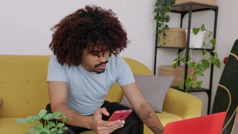 Young African American man multitasking with laptop and smartphone at home 스톡 동영상 345095638