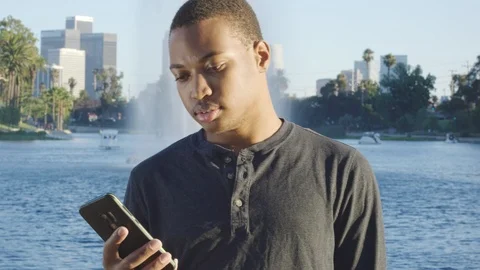 Young african american man using his cellphone in front of lake Stock Footage 119335837