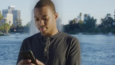 Young African american man using his cellphone in front of lake Stock Footage 119336613