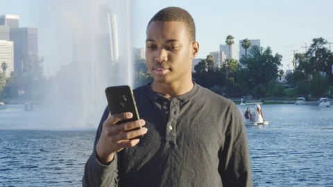 Young African american man using his phone, looking around in front of lake Stock Footage 119336688